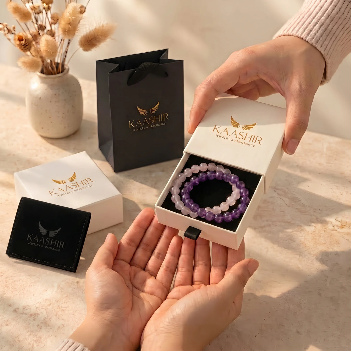 Kaashir amethyst and rose quartz bracelet set in a gift box being handed over, with gift bag and pouch