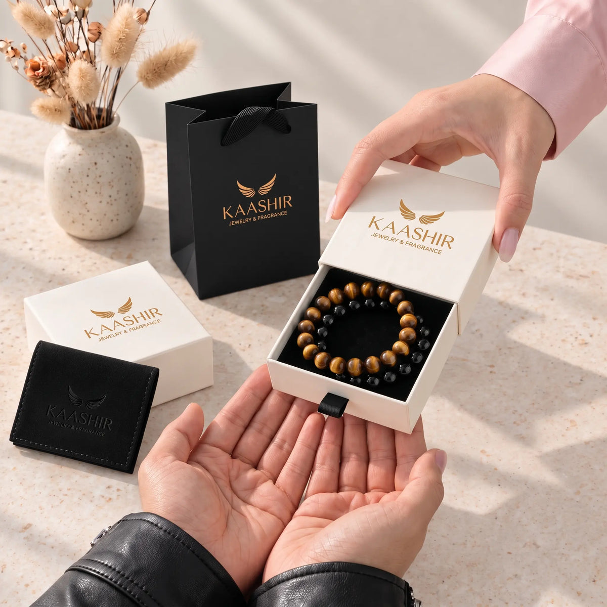 Kaashir black obsidian and tiger eye bracelet set in a gift box being handed over, with gift bag and pouch