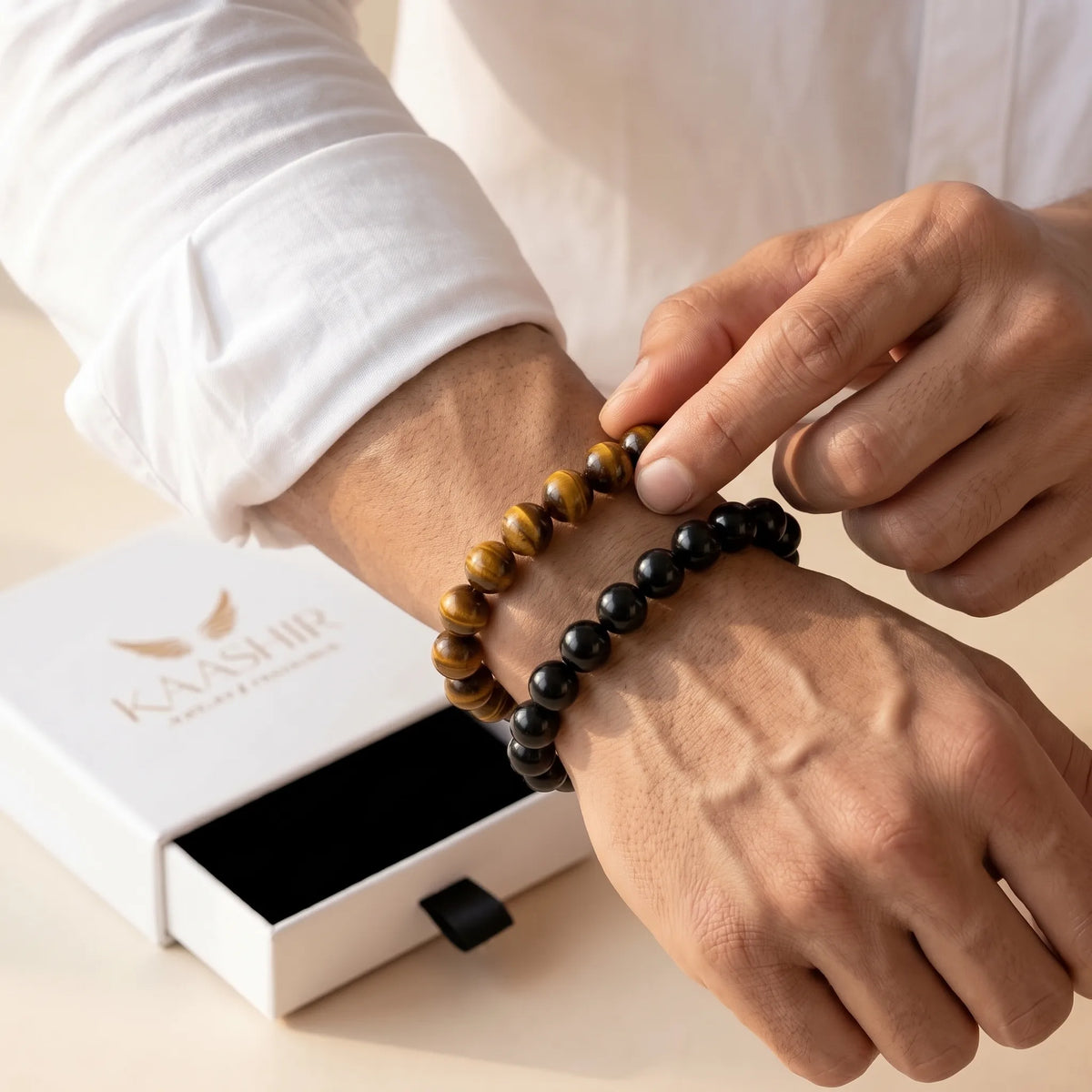 Man putting on Kaashir tiger eye and black obsidian bracelets beside an open gift box