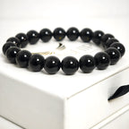Top-down flat lay view of a minimalist black obsidian bead bracelet on a marble surface.