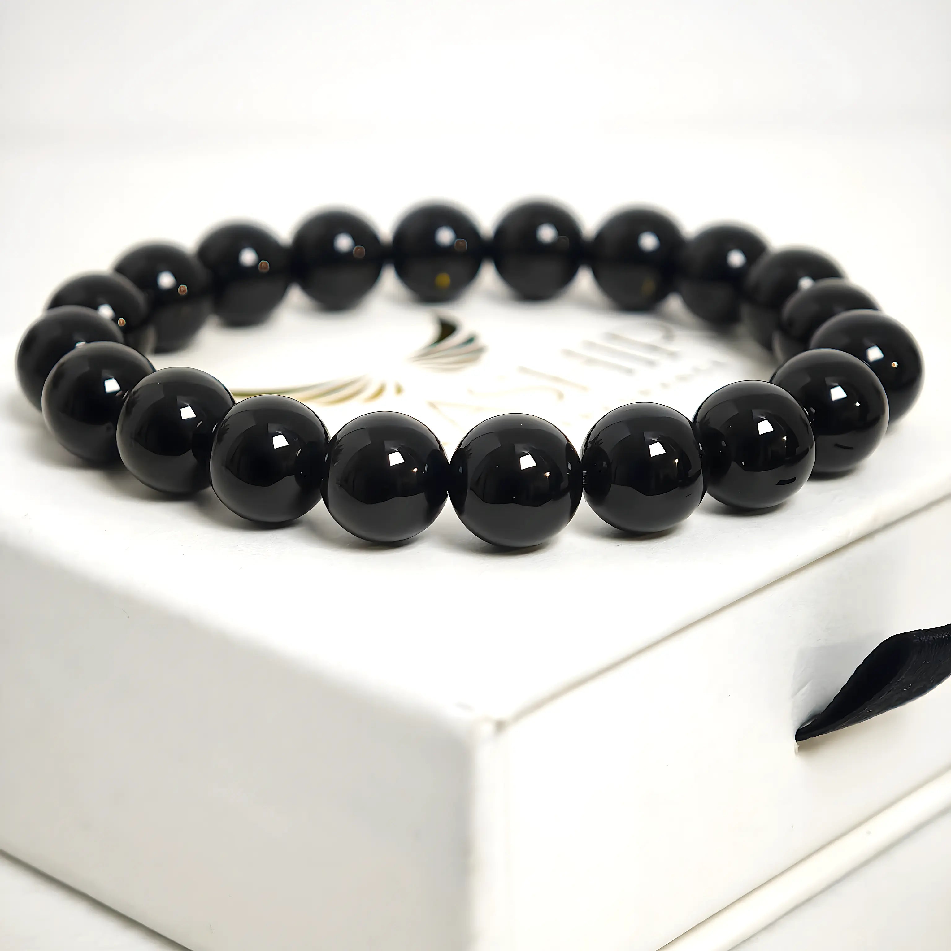 Top-down flat lay view of a minimalist black obsidian bead bracelet on a marble surface.
